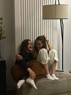 two women sitting on a couch with their arms around each other and one holding her head