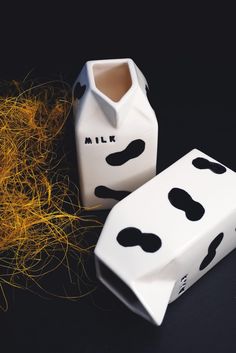 two milk cartons with black and white designs on them sitting next to some dry grass