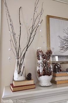 two vases with branches and pine cones on a mantle