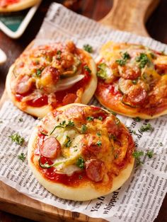 three small pizzas sitting on top of a wooden cutting board