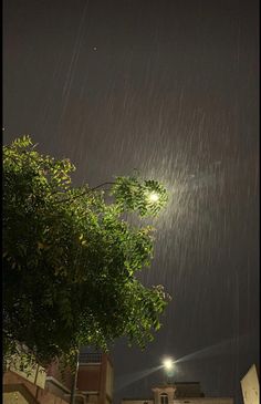 the street light shines brightly in the dark night sky above some trees and buildings