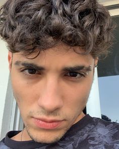 a close up of a person with curly hair and piercings on his forehead looking at the camera