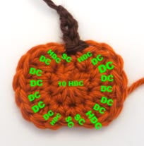 an orange crocheted pumpkin ornament with green letters on it's side