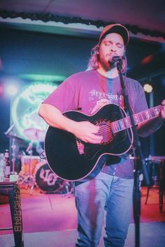 a man standing in front of a microphone while holding a guitar