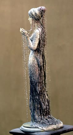 a statue of a woman with long hair and beads on her head is shown in front of a brown background