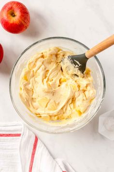 an apple and cream mixture in a bowl next to two apples on a white surface