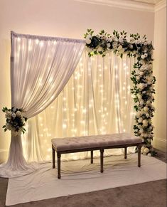 a wedding ceremony setup with white flowers and greenery on the wall, along with a bench