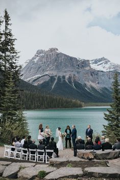 a group of people standing next to each other near a lake with mountains in the background