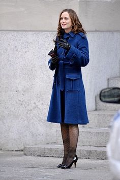 a woman in a blue coat is standing on the street