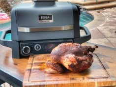 a turkey sitting on top of a wooden cutting board next to an electric bbq