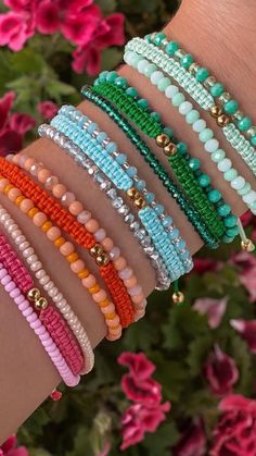 a woman's arm with several bracelets on it and flowers in the background