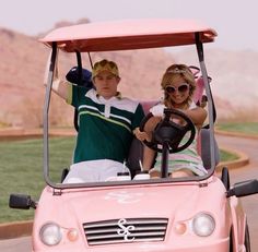 a man and woman riding in the back of a pink golf cart