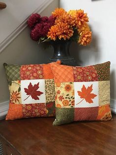 two decorative pillows on a wooden table with flowers in the vase next to each other