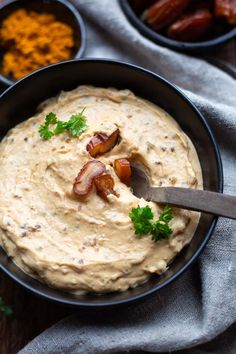 a black bowl filled with hummus and bacon on top of a gray napkin next to other bowls