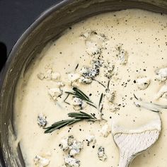 a pot filled with cheese and herbs on top of a stove burner next to a wooden spoon