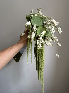 a person holding a bouquet of flowers in their hand with white blooms and green leaves