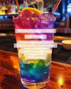 a tall glass filled with colorful liquid on top of a wooden table