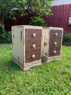 two brown and white dressers sitting in the grass next to a red barn door