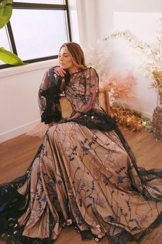 a woman in a long dress sitting on a wooden floor next to a potted plant