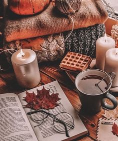 an open book on a table with candles and other items next to it, including a cup of coffee