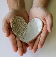 two hands holding a white heart shaped dish