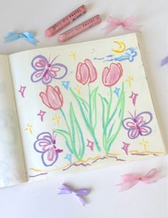 some crayons are laying next to a drawing book with flowers and butterflies on it