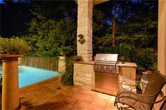 an outdoor kitchen and grill area at night with pool in the backgrouf