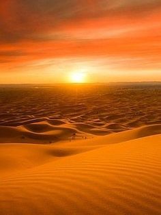 the sun is setting over an expanse of sand dunes in the distance, with some clouds