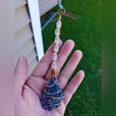 a hand holding a wire wrapped beaded necklace in it's palm, next to a house