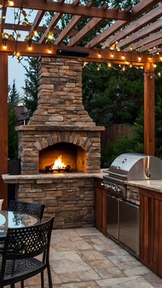 an outdoor kitchen with grill, table and lights on the outside patio at night time