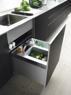 a stainless steel sink and counter in a small kitchen with trash cans on the floor