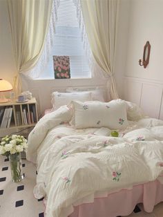 a white bed sitting next to a window covered in curtains and pink bedspread