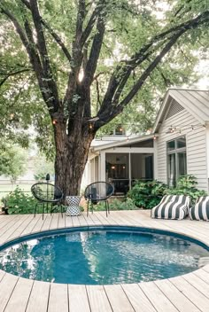 a backyard with a pool and decking area next to a large tree in front of the house