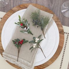 two napkins with flowers and greenery are sitting on a wooden plate next to wine glasses