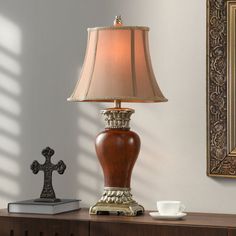 a table lamp sitting on top of a wooden dresser next to a cross and cup