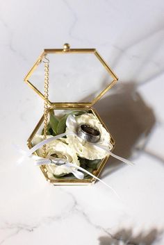 a white flower in a gold hexagonal box on a marble table with flowers