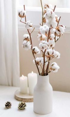 a white vase filled with cotton sitting on top of a table next to two candles