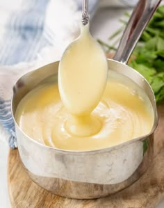 a ladle full of cheese sauce being poured into a pot with a wooden spoon