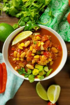 a white bowl filled with chili and corn next to limes, cilantro