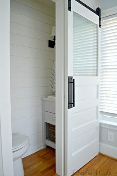 an open door leading to a bathroom with wood floors and white walls, in front of a toilet