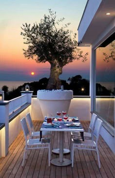 an outdoor dining area with table and chairs on the deck overlooking the ocean at sunset