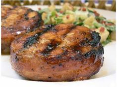 two pieces of meat sitting on top of a white plate next to a green salad