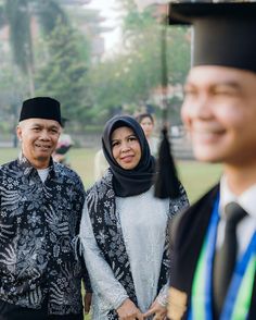 two men and a woman standing next to each other in front of a crowd wearing graduation gowns