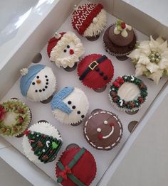 twelve decorated cupcakes in a white box with christmas decorations on the top and bottom