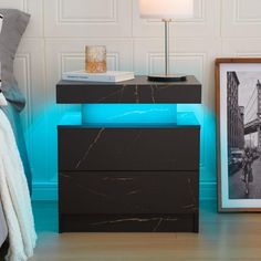 a black night stand with a blue light on it next to a bed and a framed photograph