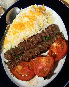 a plate with rice, meat and tomatoes on it next to a fork and knife