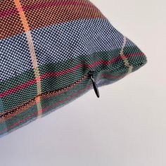 a close up of a plaid pillow on a white tablecloth with a black metal hook