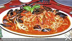 a plate of pasta with mussels and sauce on a tableclothed place mat