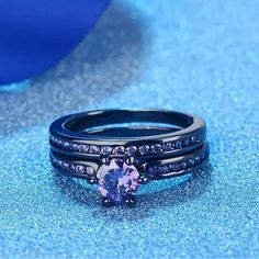 two black wedding bands with a pink diamond in the center and blue diamonds on each band