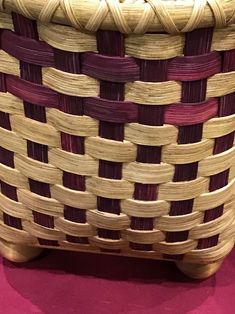 a woven basket sitting on top of a pink tablecloth covered floor next to a vase